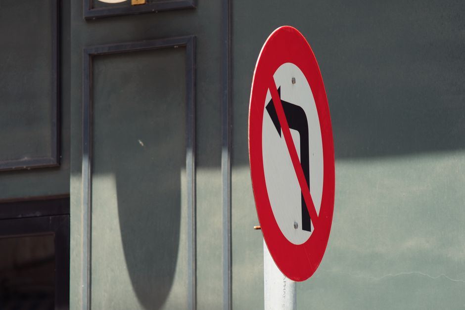 A vertical metal pole supporting a rectangular white traffic sign with a black border, indicating no parking with a red circle and diagonal line crossing out a black letter 'P', and an orienting black arrow pointing to the right. The sign is mounted against a bright blue sky with a few wispy clouds. The image captures a clear outdoor setting, typical of urban areas where house removals and furniture transport may occur, with the sign potentially indicating parking restrictions relevant to moving logistics. The sign’s placement on the pavement suggests a location near a property entrance or street, highlighting the importance of checking local parking rules during home relocation or moving processes, an aspect that Man with Van Bexleyheath helps clients manage through professional removals services.
